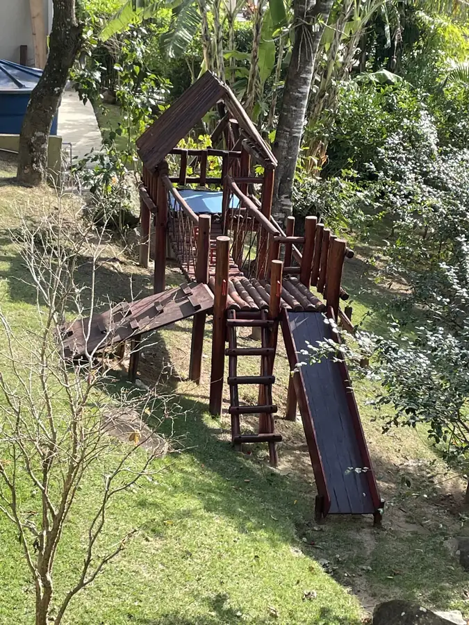 Playground de madeira com rampa de escalada e escorregador integrado à vegetação de uma chácara