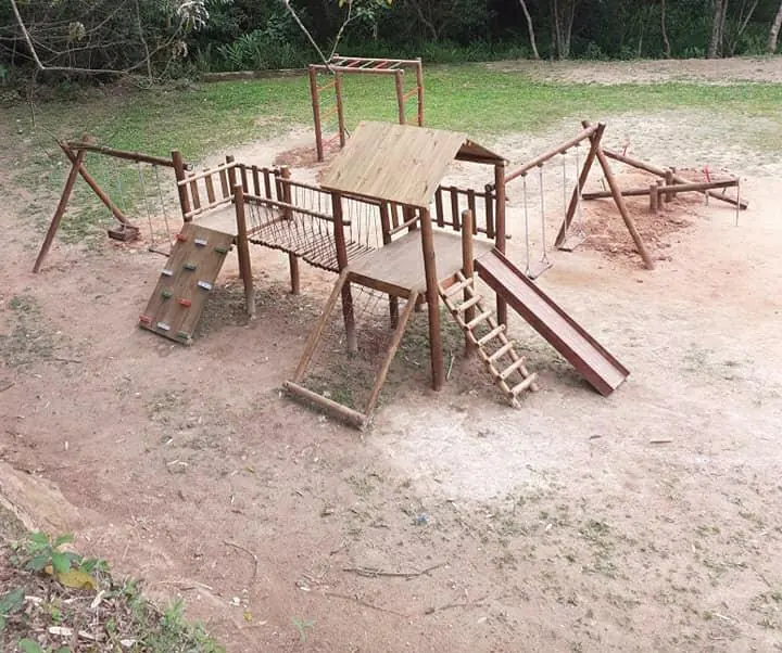 Playground de madeira em chácara com plataforma, escadas e escorregador sobre terreno de terra