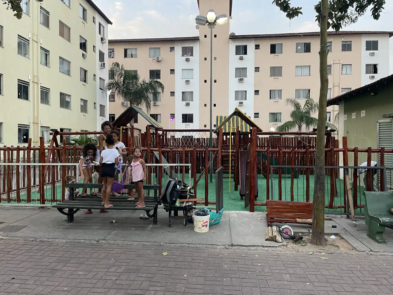 Playground de madeira em condomínio com crianças brincando ao fundo
