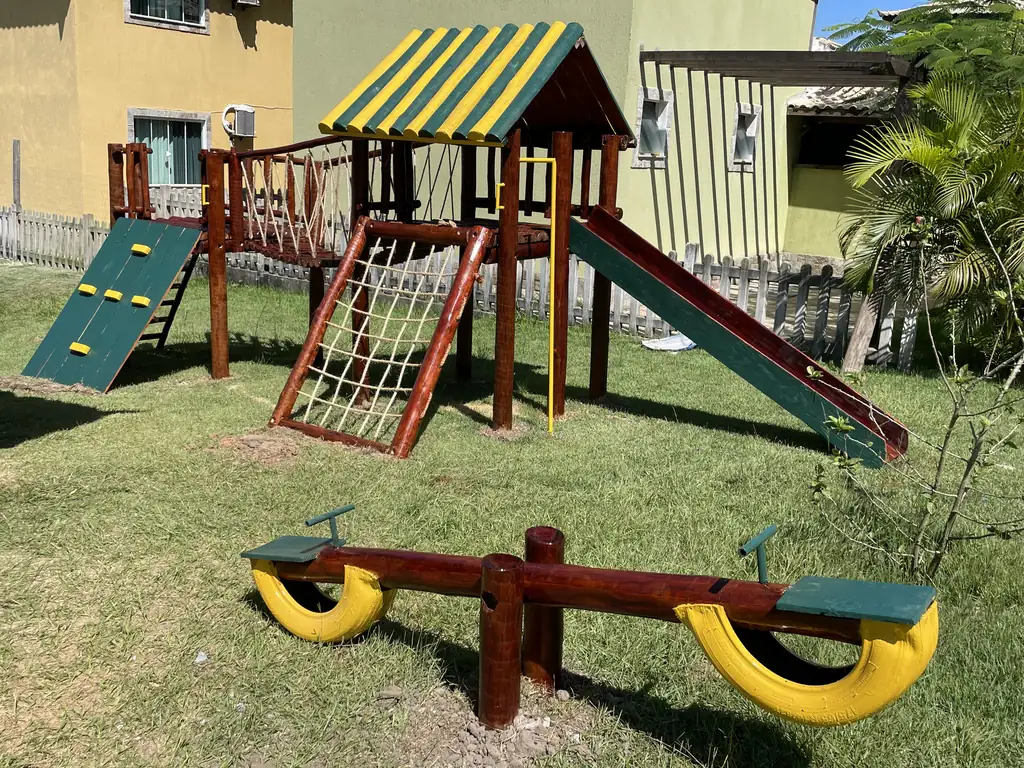 Playground de madeira com torre coberta, escorregador, rede de escalada e gangorra no gramado de um condomínio residencial