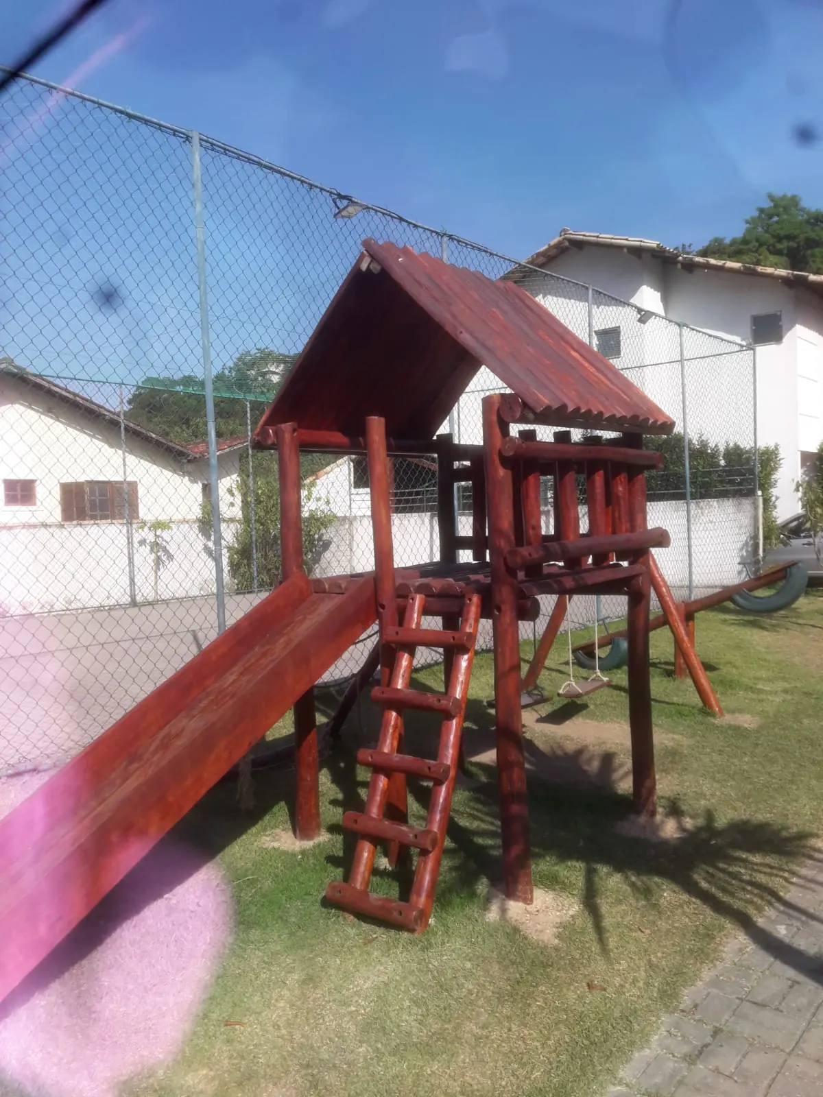 Playground de madeira com torre coberta e escorregador no gramado de condomínio