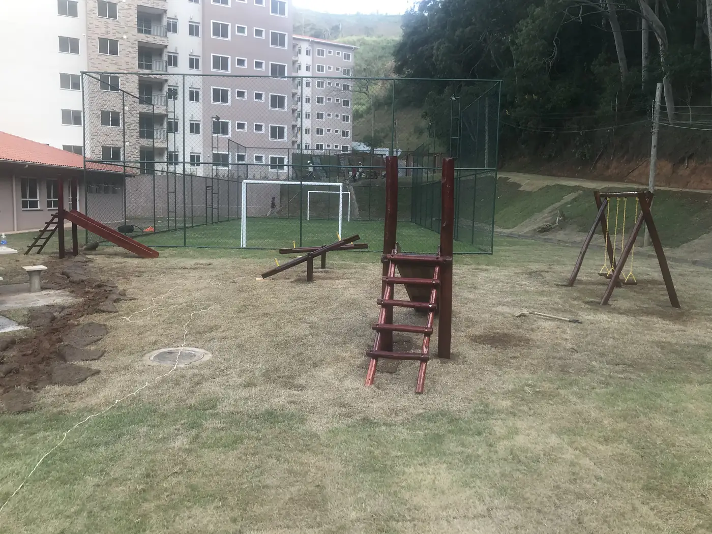 Playground de madeira PHD em instalação no gramado de condomínio residencial, com escorregador, gangorra, escada e balanço já posicionados