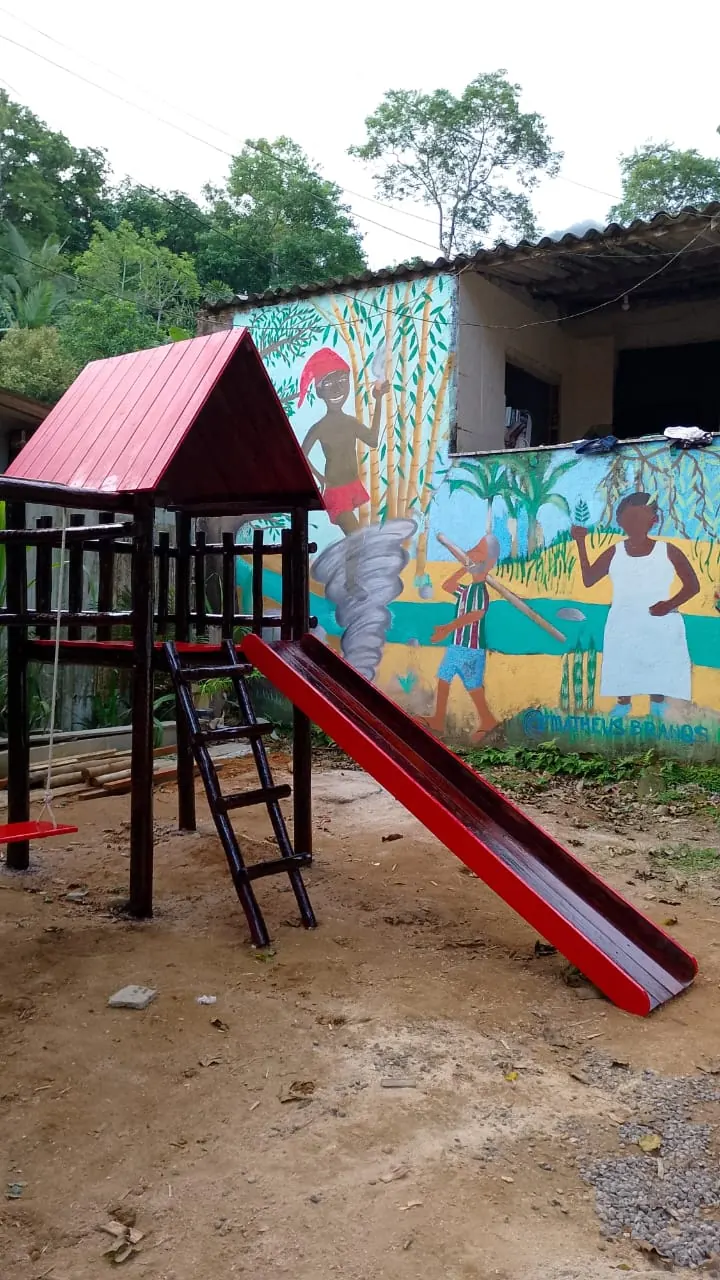 Playground de madeira com torre coberta e escorregador na área externa de uma escola com muro pintado