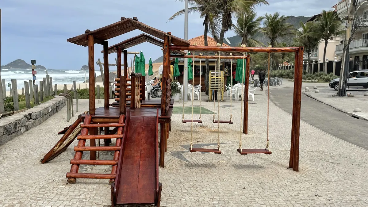 Parquinho de madeira reformado pela PHD Playground ao lado de um quiosque à beira-mar, com escorregador, escalada, ponte e balanços